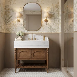 May include: A bathroom vanity featuring a white marble countertop with a brass faucet and handles, set atop a wooden cabinet with two doors and a lower shelf. Above the vanity is an oval mirror flanked by two wall sconces with white shades.