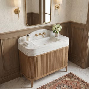 Angled view of a bespoke Carrara marble vanity featuring a seamless integrated sink, premium white marble with subtle gray veining, brushed brass wall-mounted faucet, fluted natural oak cabinet, and refined architectural details. This handcrafted bathroom vanity blends timeless natural stone with warm wood textures for upscale residential interiors.
