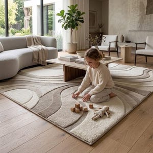 Cream and beige organic wave area rug styled in a luxury modern living room with a curved cream sofa, walnut coffee table, neutral lounge chairs, indoor greenery and warm natural wood flooring.