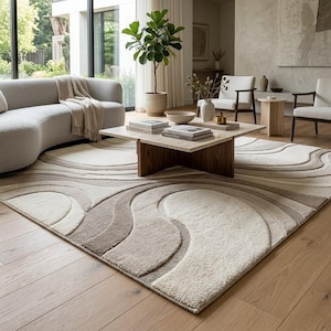 Premium cream and beige abstract wave area rug with flowing sculpted organic shapes, styled in a sophisticated modern living room with a curved cream sofa, walnut coffee table, natural wood flooring and indoor greenery.