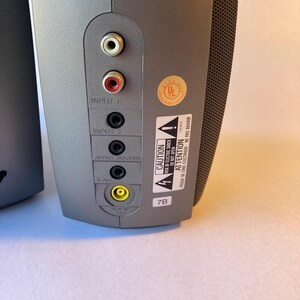 May include: A gray speaker back panel featuring Input 1 with white and red RCA ports, Input 2, Output Woofer, and a yellow DC power port. A UL certification sticker and a black and white caution label with text in English and French are visible.