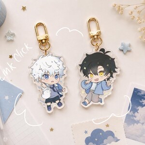 Peut inclure: Deux porte-clés en acrylique représentant des personnages de style anime avec des fermoirs mousquetons dorés. Un personnage a les cheveux blancs et les yeux bleus, l'autre les cheveux noirs et les yeux jaunes. Le texte Link Click est visible.