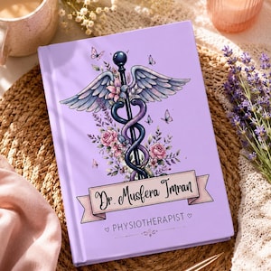 May include: A light purple hardcover notebook featuring a central caduceus symbol entwined with pink roses and lavender sprigs, surrounded by small butterflies. A banner displays the text Dr. Musfera Imran and the word PHYSIOTHERAPIST.