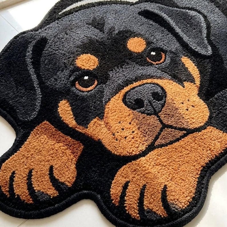 May include: A tufted rug shaped like a Rottweiler dog head and front paws. The rug features a black and tan color palette with a textured, plush surface. The dog has large brown eyes, a black nose, and tan markings above the eyes and on the muzzle.