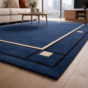 May include: A rectangular area rug featuring a deep blue field with a cream-colored border and thin black accent lines. The design includes cream-colored square corner accents and a central rectangular frame pattern across the surface.