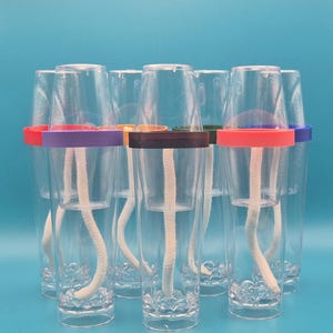 May include: A set of clear plastic self-watering planters, each featuring a transparent cup insert, a white cotton wick extending into the base, and a distinctively colored plastic ring in red, purple, orange, brown, green, or blue.
