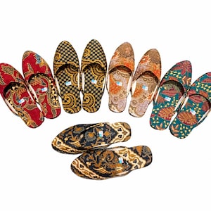 Puede incluir: Cinco pares de zapatillas sin cordones con varios patrones estilo batik en rojo, negro, dorado, naranja y verde azulado. Cada zapatilla tiene una punta afilada y una pequeña etiqueta azul en el talón. El calzado está dispuesto en semicírculo.