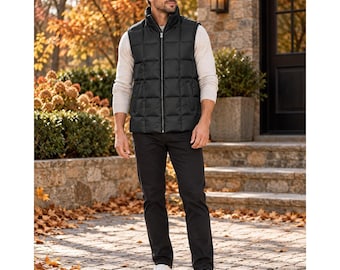 Op de afbeelding: Een zwart gewatteerd vest met een volledige ritssluiting aan de voorzijde, gedragen over een crèmekleurige trui met lange mouwen, gecombineerd met een donkere broek en witte sneakers. Het vest heeft een ruitvormig stikpatroon.