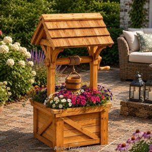 Peut inclure: Un puits décoratif en bois servant de jardinière, doté d'une base carrée à panneaux entrecroisés, d'un toit en bardeaux et d'une manivelle centrale avec une corde retenant un petit seau suspendu, rempli de fleurs aux tons roses, violets et blancs.