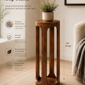 Op de afbeelding: Een hoge, ronde bijzettafel van massief walnoothout met een gladde, natuurlijke afwerking. De tafel heeft een cilindrisch ontwerp met vier verticale steunpoten en een rond tafelblad. Een kleine groene plant staat op de tafel.