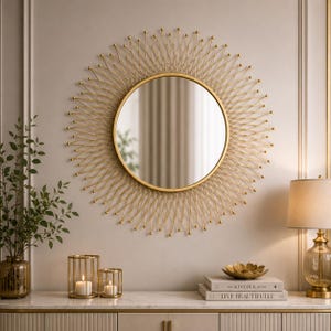 May include: A round wall mirror featuring a gold-toned sunburst frame with thin metal spokes radiating from the center. The mirror has a smooth circular glass surface surrounded by a thin gold rim, creating a star-like pattern on the wall.