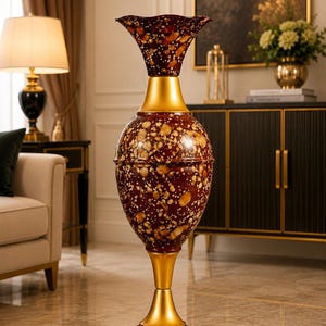 May include: A tall floor vase featuring a dark burgundy and brown speckled pattern with a glossy finish. The vase has a flared, ruffled rim, a bulbous central body, and a circular base, all accented with smooth, matte gold-toned metal sections.