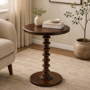 Pode incluir: Uma mesa lateral redonda de madeira castanho-escura com um tampo circular liso e uma base central de pedestal com um design de anéis empilhados. A mesa assenta numa base circular e suporta um vaso branco e dois livros empilhados com texto.