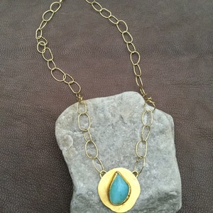 May include: A gold chain necklace with a teardrop-shaped turquoise stone set in a gold pendant.