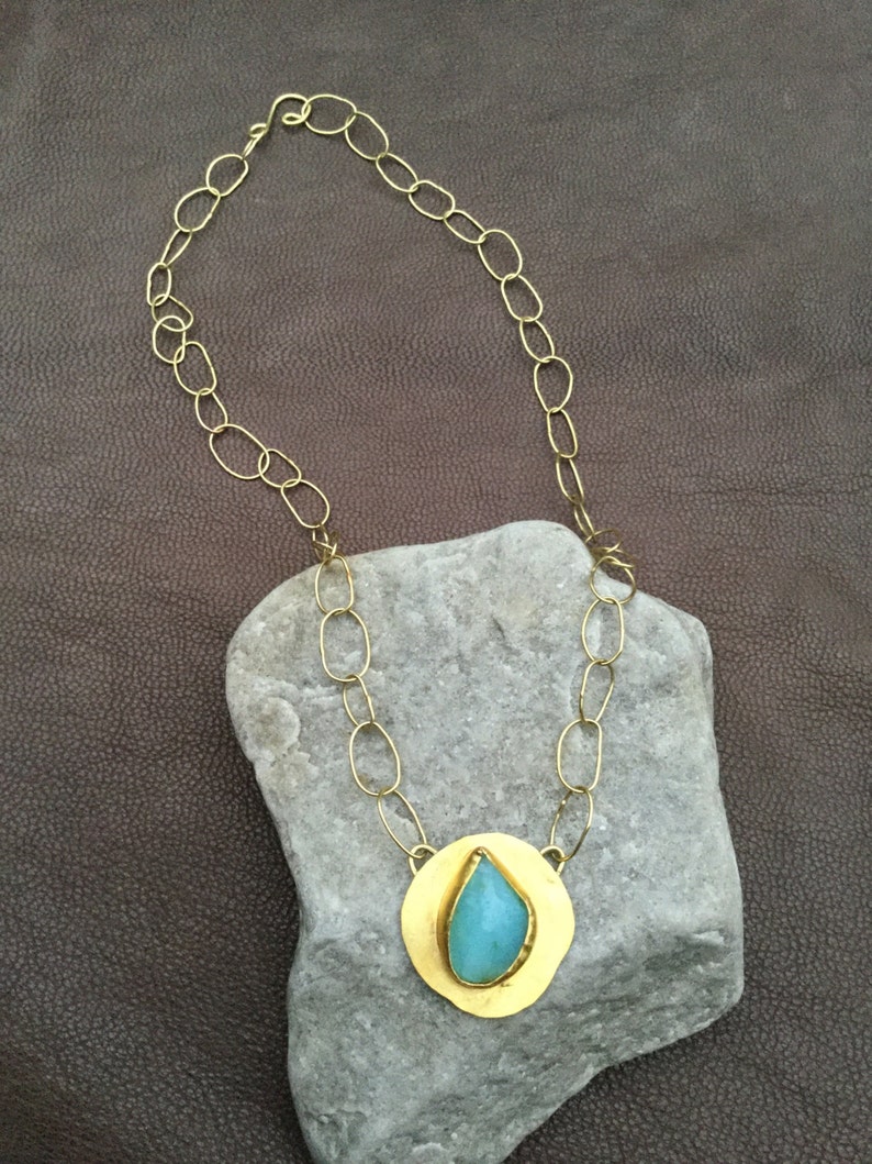 May include: A gold chain necklace with a teardrop-shaped turquoise stone set in a gold pendant.