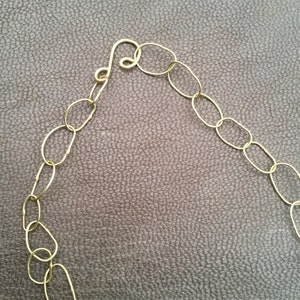 May include: A gold chain necklace with oval links and a clasp. The chain is on a brown textured surface.