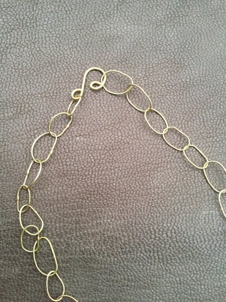 May include: A gold chain necklace with oval links and a clasp. The chain is on a brown textured surface.