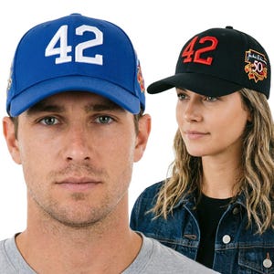 Puede incluir: Una gorra de béisbol azul con el número 42 bordado en blanco en la parte frontal y una gorra de béisbol negra con el número 42 en rojo en la parte frontal, con un parche del 50 aniversario de Jackie Robinson en el lateral de la gorra negra.