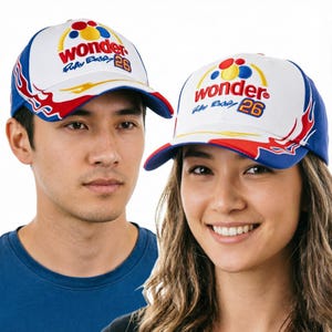 Puede incluir: Una gorra de béisbol blanca con paneles laterales azules y detalles de llamas rojas en la visera. El frente presenta la palabra wonder en rojo, una firma azul, el número 26 en naranja y un gráfico de círculos rojos, azules y amarillos.