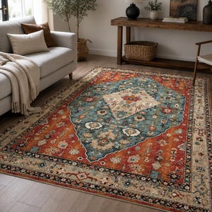 Peut inclure: Un tapis rectangulaire orné d'un médaillon central en forme de losange crème, entouré d'un large champ bleu sarcelle et d'une bordure orange brûlé. Le motif présente des détails floraux et géométriques complexes en bleu, rouge et beige.