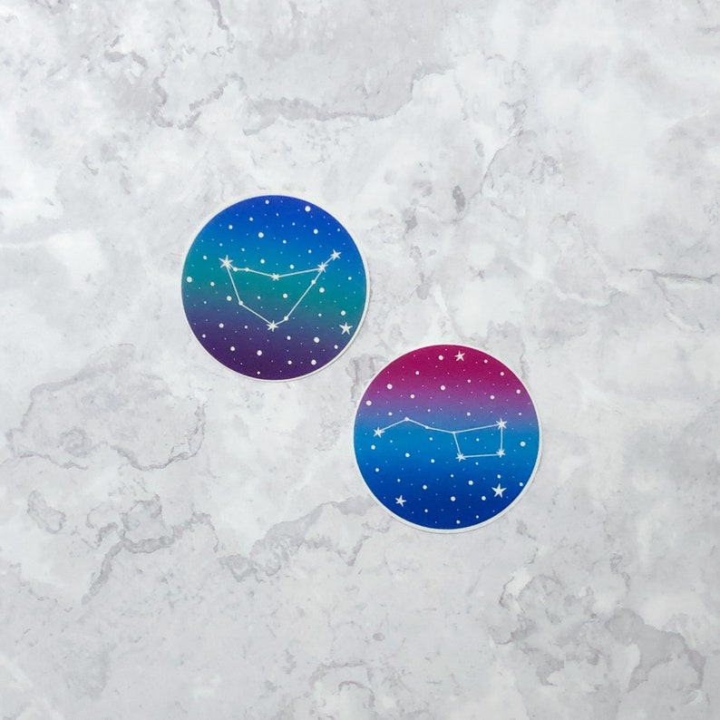 May include: Two round stickers with a galaxy background and white constellation outlines. The top sticker features the constellation Capricorn, while the bottom sticker features the constellation Ursa Major.