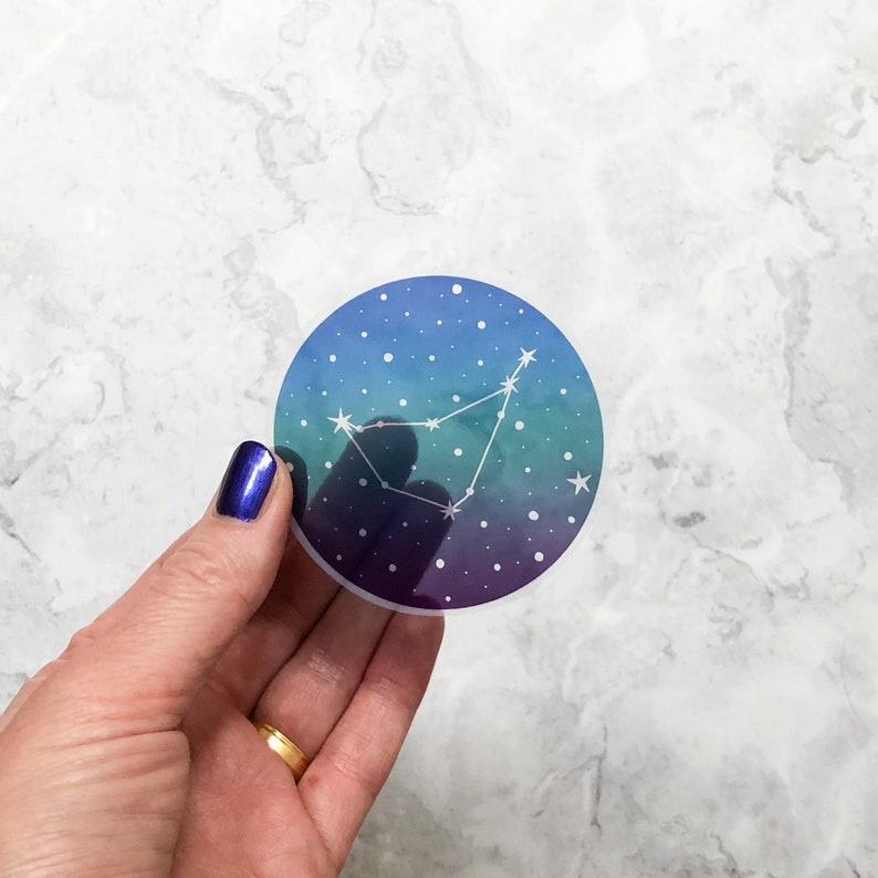 May include: A round sticker with a blue, green, and purple ombre background. The sticker features a white outline of the Capricorn constellation with white stars.