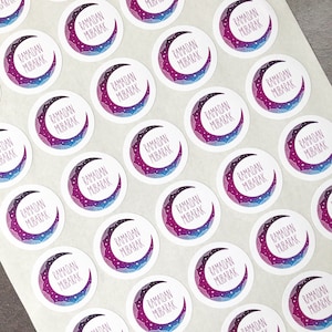 May include: A sheet of round stickers with a crescent moon design. The moon is purple and blue with white stars. The text "Ramadan Mubarak" is written in white on the moon.