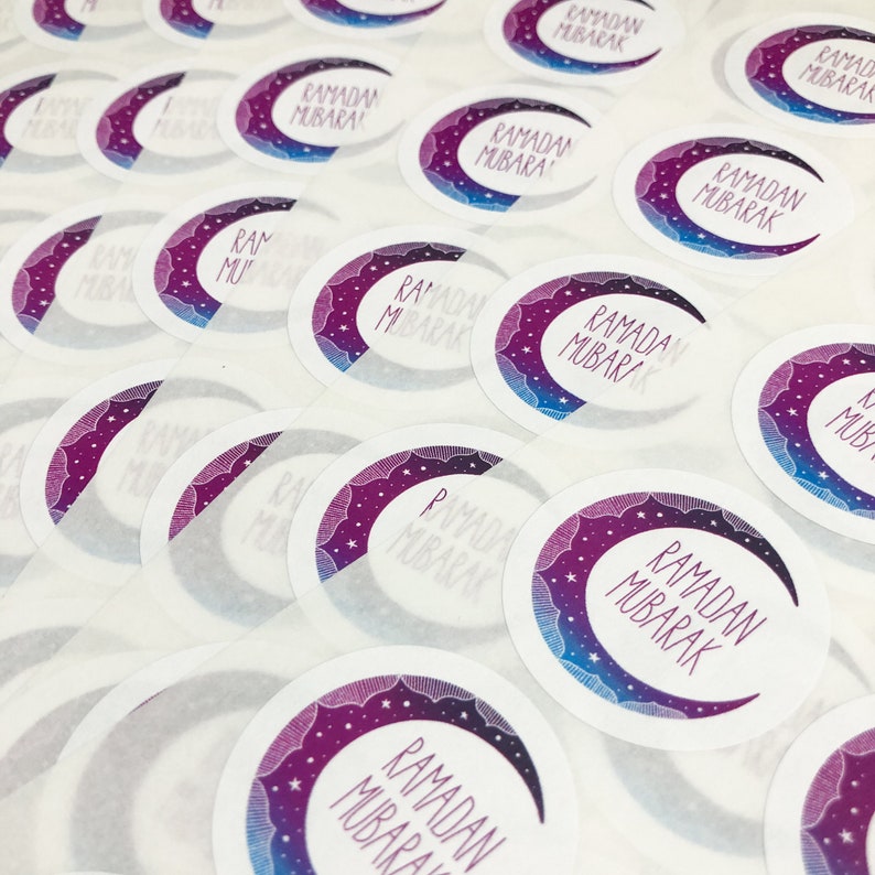 May include: A sheet of round stickers with a crescent moon and stars design. The stickers are white with a purple and blue gradient. The text "Ramadan Mubarak" is written on each sticker.