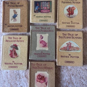 May include: A collection of seven vintage Beatrix Potter books with tan and grey covers, featuring titles such as The Tale of Peter Rabbit, Ginger & Pickles, Squirrel Nutkin, Benjamin Bunny, Jemima Puddle-Duck, The Flopsy Bunnies, and Mrs. Tiggy-Winkle.