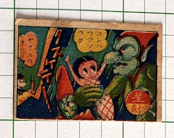 May include: A rectangular vintage-style card featuring a colorful illustration of a green-skinned creature with a large nose holding a small character with black hair. The scene includes yellow speech bubbles with Japanese text and a red circular emblem.