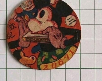 May include: A circular cardboard pogs disc featuring a vintage cartoon character playing a harmonica. The design includes orange, black, and green colors, with the text 20671 printed in yellow at the bottom and Japanese characters on the left side.