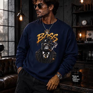 May include: A navy blue long-sleeve sweatshirt featuring a graphic print of a gorilla wearing a black fedora, sunglasses, and a suit, with the word BOSS in gold lettering above the gorilla and a trail of smoke rising from a cigar.