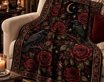 May include: A black throw blanket featuring a detailed pattern of deep red roses, green foliage, and two black ravens perched on branches. The design includes a golden crescent moon and stars, finished with a decorative floral border along the edges.