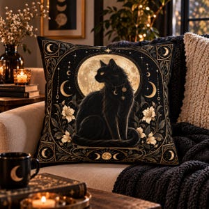 May include: A square throw pillow featuring a black cat sitting in front of a large full moon. The design includes gold celestial motifs, stars, and white flowers on a black background, framed by a decorative border with crescent moon phases.