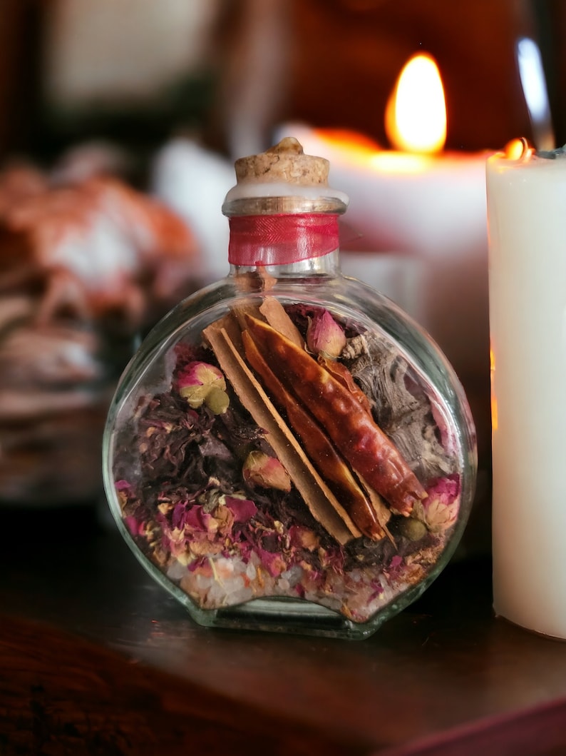 May include: A clear glass bottle with a cork stopper filled with dried herbs, spices, and rose petals. The bottle is sitting on a wooden surface.