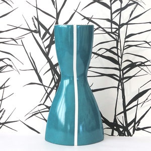 Könnte beinhalten: Eine tealblaue Keramikvase mit einem weißen Streifen in der Mitte. Die Vase hat einen breiten Boden und einen schmalen Hals, was ihr eine Sanduhrform verleiht.