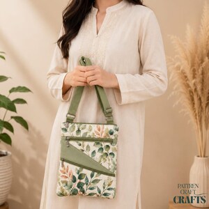 May include: A crossbody bag featuring a botanical print of green and orange leaves on a cream background. The bag has an adjustable olive green strap, a matching olive green triangular front pocket, and two silver-toned zipper closures.