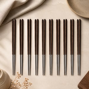 May include: A set of nine pairs of chopsticks arranged in a row. Each pair features a dark brown wooden upper handle and a smooth, silver-toned metal lower tip. The chopsticks are uniform in design, showcasing a clean transition between the wood and metal sections, creating a functional and balanced appearance for dining.
