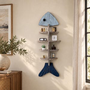 May include: A wall-mounted fish skeleton shelf featuring a light blue head with a black eye, a dark blue tail, and four horizontal shelves attached to a central spine. The wood has a distressed, weathered finish in shades of white and brown.