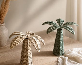 Könnte beinhalten: Zwei dekorative Palmenskulpturen aus geflochtenen Naturfasern. Eine Skulptur ist in hellem Beige gehalten, die andere in einem gedämpften Salbeigrün. Beide verfügen über einen konischen Stamm und ausladende Palmwedel aus geflochtenem Material.