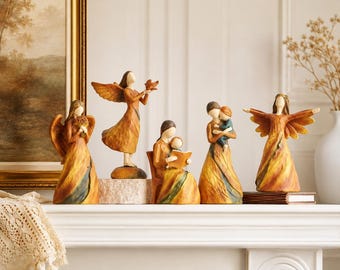 Könnte beinhalten: Ein Set aus fünf handbemalten Harzfiguren mit gesichtslosen Gestalten in fließenden Gewändern in Bernstein, Gold und dunklem Blaugrün. Die Gruppe umfasst zwei geflügelte Engel, eine sitzende Figur beim Vorlesen und zwei Umarmungsszenen.