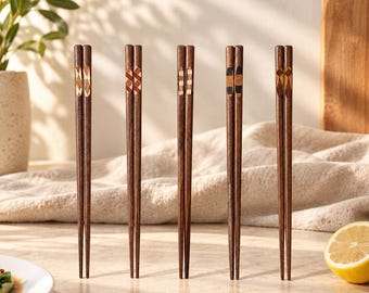 Könnte beinhalten: Fünf Paar dunkelbraune Essstäbchen aus Holz, die aufrecht stehen. Jedes Paar weist im oberen Bereich ein einzigartiges geometrisches Intarsienmuster auf, darunter Rauten-, Schachbrett- und Rechteckdesigns in verschiedenen Holztönen.