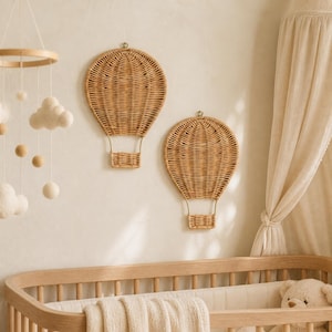Puede incluir: Dos decoraciones de pared con forma de globo aerostático hechas de ratán tejido de color marrón claro. Cada pieza presenta una forma de globo redondeada con una pequeña cesta rectangular unida en la parte inferior por soportes de alambre.