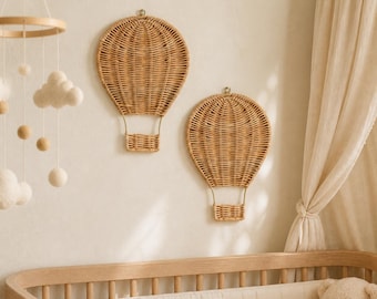 Könnte beinhalten: Zwei Wanddekorationen in Form von Heißluftballons aus hellbraunem geflochtenem Rattan. Jedes Stück besteht aus einer abgerundeten Ballonform mit einem kleinen rechteckigen Korb, der unten mit dünnen Drahtstützen an einer neutralen Wand befestigt ist.