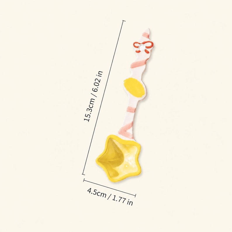 May include: A ceramic spoon with a star-shaped bowl in yellow and a white handle featuring pink stripes, a yellow oval accent, and a red bow detail at the top. The spoon measures 6.02 inches in length and 1.77 inches in width at the star bowl.