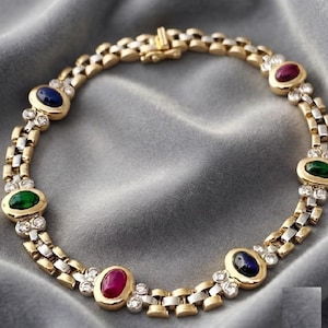 May include: A gold and silver link bracelet featuring alternating oval cabochon gemstones in red, blue, and green. The bracelet is accented with small, clear round stones set between each coloured gemstone and includes a secure metal clasp closure.