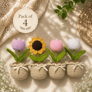 Könnte beinhalten: Ein Set aus vier gehäkelten Topfblumen, bestehend aus einer lavendelfarbenen Tulpe, einer gelben Sonnenblume, einer rosa Tulpe und einer weißen Tulpe. Jede Blume steckt in einem beigen Häkeltopf mit einer kleinen weißen Schleife. Text Pack of 4.