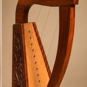 Puede incluir: Un arpa de madera con cuello curvo, caja de resonancia con diez cuerdas verticales y un panel lateral decorado con tallas florales intrincadas. El instrumento tiene un acabado marrón pulido y clavijas de afinación plateadas en el marco.