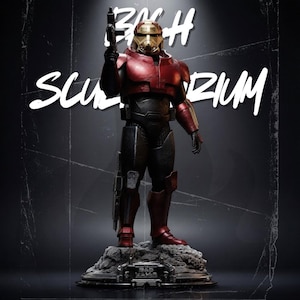 Peut inclure: Une figurine blindée debout en plaques rouges et noires avec un casque doré, tenant un blaster dans une main. La figurine repose sur une base rocheuse grise texturée avec le texte BAD WALER visible. L'arrière-plan affiche le texte BACH SCULPTORIUM.