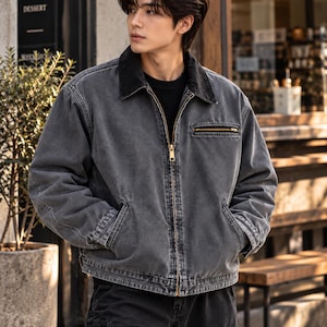May include: A charcoal gray denim jacket featuring a black corduroy collar, a full-length brass-toned front zipper, and a single horizontal zippered chest pocket. The jacket has long sleeves with buttoned cuffs and two lower side pockets.